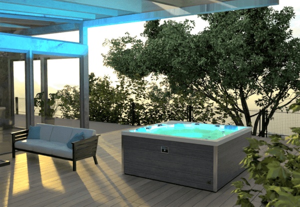 Outdoor Whirlpool Infinitas Blueline 500 mit LED-Beleuchtung und Wasserfall auf Terrasse umgeben von Gartenbäumen.