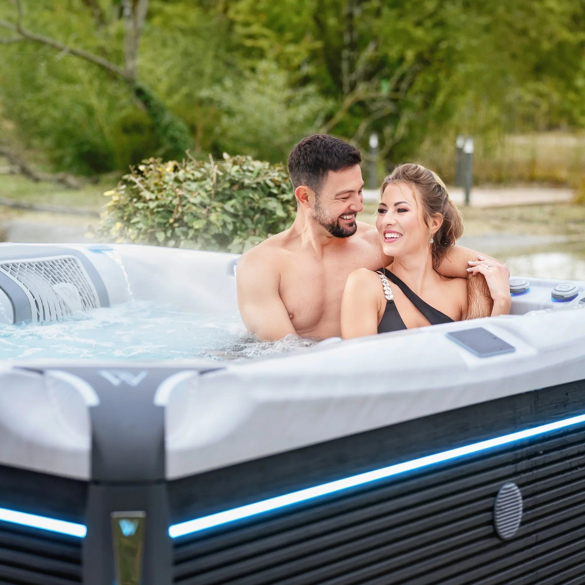 Paar entspannt im Wellis Outdoor Whirlpool auf moderner Terrasse mit Garten, luxuriöse Wellness-Atmosphäre